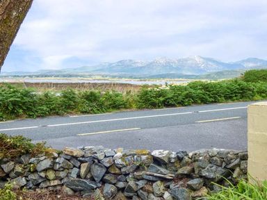A stone wall with a road behind it and a mountain range in the background at Ti Sheamuis in Cashel near Carna County Galway