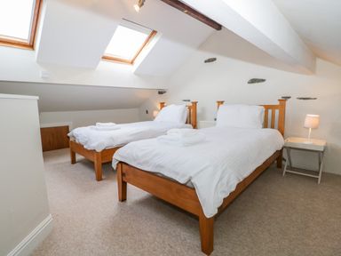 A bedroom with two single beds wooden frames white bedding a side table with a lamp and skylight windows at Fishers Retreat in Bowness-On-Windermere