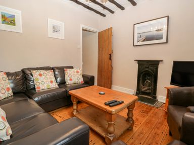 A living room with black leather sofas and colorful cushions a wooden coffee table a small black fireplace a wooden door and a television at Fishers Retreat in Bowness-On-Windermere