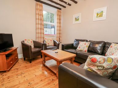 A living room with leather sofas and armchairs around a wooden coffee table and a television on a wooden stand at Fishers Retreat in Bowness-On-Windermere
