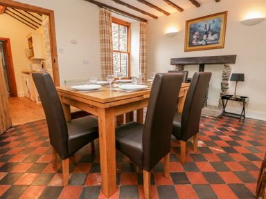 A dining room with a wooden table and four chairs set with plates and glasses at Fisher's Retreat in Bowness-On-Windermere