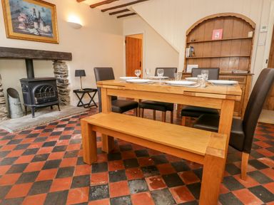 A dining room with a wooden table, bench, chairs, a stove in a stone fireplace, and a wooden cabinet at Fishers Retreat in Bowness-On-Windermere