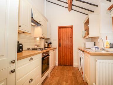 A kitchen with wooden countertops white cabinets a washing machine and a wooden door at Fishers Retreat in Bowness-On-Windermere