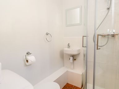 A bathroom with a toilet, wall-mounted sink, shower enclosure, and a toilet paper holder at Fishers Retreat in Bowness-On-Windermere