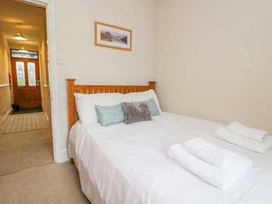 A bedroom with a wooden bed frame white bedding pillows and towels on the bed with a hallway and wooden door visible at Fishers Retreat in Bowness-On-Windermere