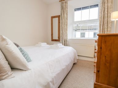 A bedroom with a bed with pillows and towels a wooden chest of drawers and a window at Fishers Retreat in Bowness-On-Windermere