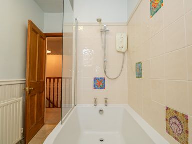 A bathroom with a bathtub shower combination and decorative tiles at Fishers Retreat in Bowness-On-Windermere