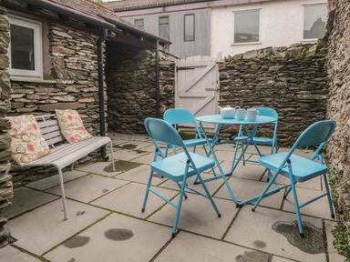 A stone walled patio with a blue metal table and chairs and a white bench with cushions at Fishers Retreat in Bowness-On-Windermere