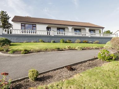 A single story house with a tiled roof a white balustrade in front and a garden with grass and bushes at Aras Iosgan in Carraroe County Galway