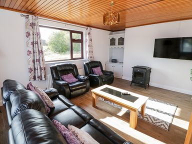 A living room with black leather sofas a wooden coffee table a wood stove and a wall-mounted tv at Aras Iosgan in Carraroe County Galway