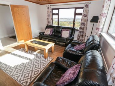 A living room with black leather sofas a wooden coffee table patterned rug and floral curtains at Aras Iosgan Carraroe County Galway