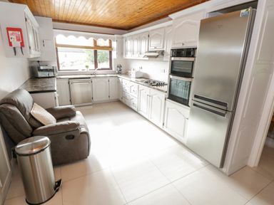 A kitchen with white cabinets a stainless steel refrigerator and double oven a gray armchair a trash bin and a window at Aras Iosgan in Carraroe County Galway