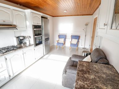 A kitchen with white cabinets a gray sofa two blue chairs a floor lamp and stainless steel appliances at Aras Iosgan in Carraroe County Galway