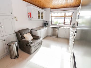 A kitchen with white cabinets a gray recliner chair a stainless steel trash can and dishwasher at Aras Iosgan in Carraroe County Galway