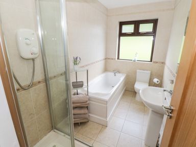 A bathroom with a shower enclosure, bathtub, toilet, pedestal sink, towels, and a window at Aras Iosgan in Carraroe County Galway
