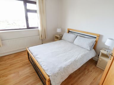A bedroom with a bed two bedside tables and lamps and a window with curtains at Aras Iosgan in Carraroe County Galway