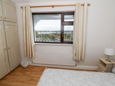 A bedroom with a window overlooking a landscape wardrobe bedside table with lamp and bed at Aras Iosgan in Carraroe County Galway