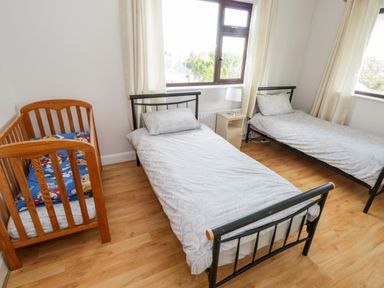 A bedroom with two single beds a wooden baby crib and a small nightstand with a lamp by the window at Aras Iosgan in Carraroe County Galway