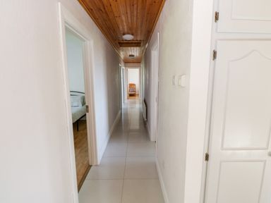 A long hallway with white tiled floor wooden ceiling and open doors leading to bedrooms at Aras Iosgan in Carraroe County Galway