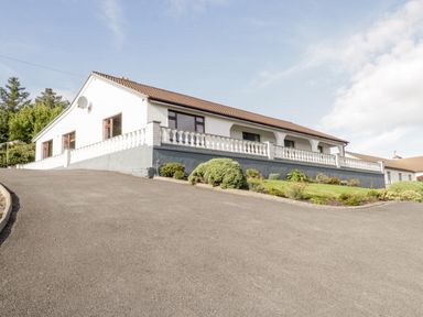 A single-story house with white exterior and tiled roof surrounded by a paved driveway and garden at Aras Iosgan in Carraroe County Galway