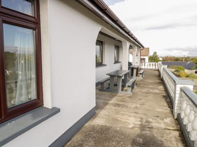 An outdoor patio area with picnic tables and benches along a white building with windows at Aras Iosgan in Carraroe County Galway