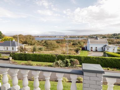 A view from a balcony over a road hedge houses and a body of water at Aras Iosgan in Carraroe County Galway