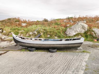 A small boat on tires near a grassy hill with rocks at Aras Iosgan in Carraroe County Galway