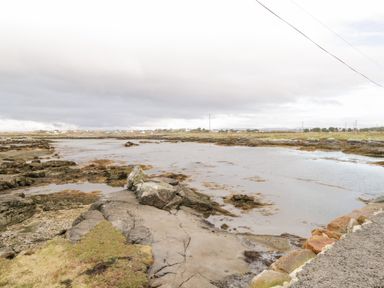 A rocky shoreline with water and distant houses under a cloudy sky at Aras Iosgan in Carraroe County Galway