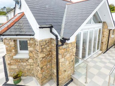 Stone exterior corner of a house with slate roofing and large glass doors on a tiled patio at Chapel Green Studio 2 Polgooth