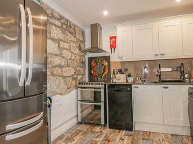 A kitchen with stainless steel fridge oven dishwasher white cabinets and stone wall at Chapel Green Studio 2 in Polgooth