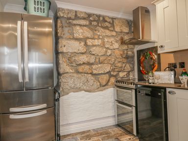 A kitchen with a stainless steel fridge oven black dishwasher exposed stone wall and kitchen cabinets at Chapel Green Studio 2 Polgooth