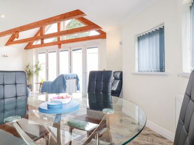 A dining area with a glass table and black chairs near large windows and wooden beams at Chapel Green Studio 2 in Polgooth