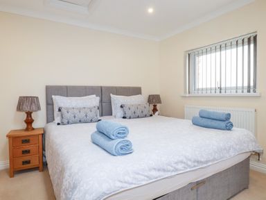 A bedroom with a large bed with white bedding blue towels on top bedside tables with lamps and a window with vertical blinds at Chapel Green Studio 2 in Polgooth
