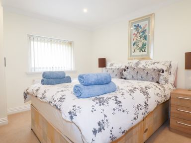 A bedroom with a bed covered in floral bedding and blue towels on top next to a wooden nightstand with lamps at Chapel Green Studio 2 in Polgooth