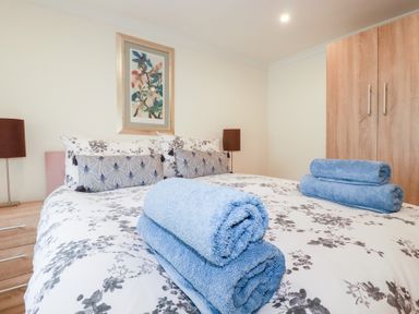 A bedroom with a bed with floral bedding and folded blue towels a wooden wardrobe and bedside tables at Chapel Green Studio 2 in Polgooth