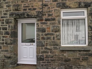 A white door and a window with lace curtains set in a stone wall of a building at Rowan Cottage in Builth Wells