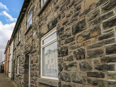 Stone exterior wall of a house with two windows and wires on the wall on a street