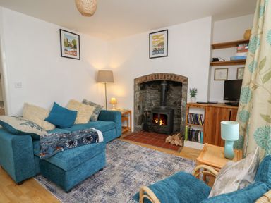 A living room with a blue sofa and armchair a wood burning stove and wooden shelves at Rowan Cottage in Builth Wells