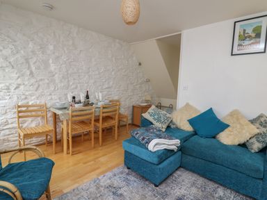 A dining area with wooden chairs and table next to a blue sofa with cushions in a living room at Rowan Cottage in Builth Wells