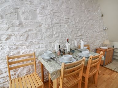 A dining table set for four with wooden chairs against a white stone wall at Rowan Cottage in Builth Wells