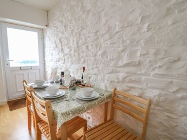 A dining area with a wooden table and chairs set for four people near a door with a stone wall at Rowan Cottage in Builth Wells