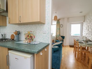 A kitchen counter with wooden cabinets and a small fridge next to a dining area with a wooden table and chairs at Rowan Cottage in Builth Wells