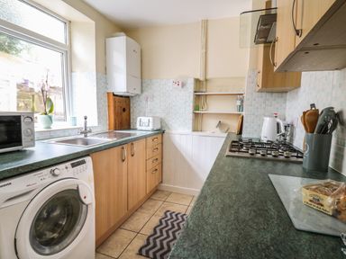 A kitchen with a washing machine microwave toaster sink gas stove kettle utensils and shelves at Rowan Cottage in Builth Wells