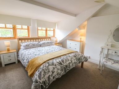 A bedroom with a double bed floral bedding and yellow throw in front of three windows with blinds and two bedside tables with lamps at Rowan Cottage in Builth Wells