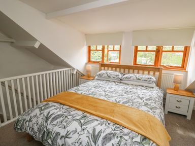 A bedroom with a bed with floral bedding and yellow throw and two bedside tables with lamps at Rowan Cottage in Builth Wells