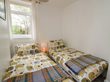 A bedroom with two single beds with sheep patterned bedding and a small lamp between them at Rowan Cottage in Builth Wells