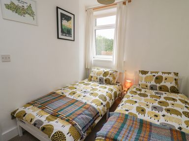 A bedroom with two single beds with sheep patterned bedding and a window with curtains at Rowan Cottage in Builth Wells
