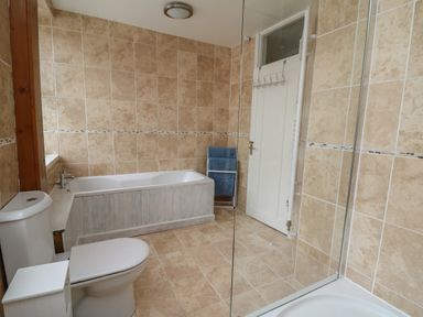 A bathroom with a toilet bathtub shower and towels at Rowan Cottage in Builth Wells
