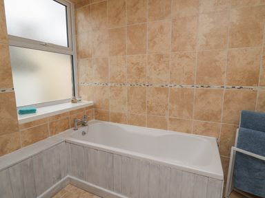 A bathroom with a white bathtub beige tiled walls and a frosted window at Rowan Cottage in Builth Wells