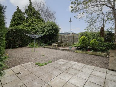 A backyard with a gravel area, patio tiles, a rotary clothesline, picnic table, and surrounding trees and shrubs at Rowan Cottage in Builth Wells